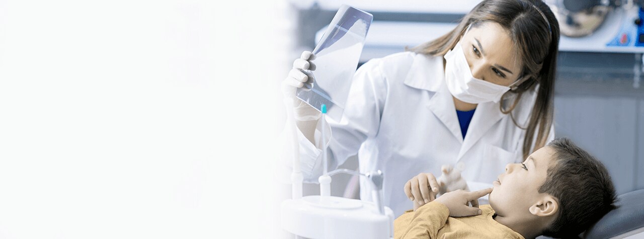 A dental professional wearing safety PPE gear and white lab coat smiling compassionately