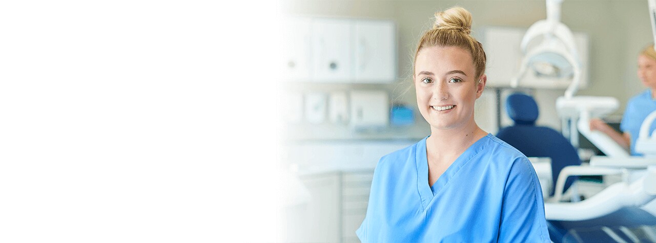 A dental professional wearing safety PPE gear and white lab coat smiling compassionately